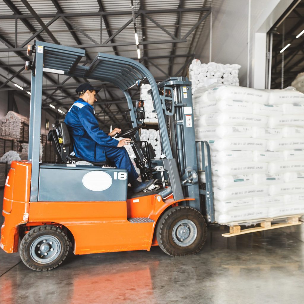 A man on a forklift works in a large warehouse, unloads bags of raw materials.
